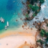 A stunning aerial view of boats anchored by a turquoise beach, showcasing a scenic coastline.