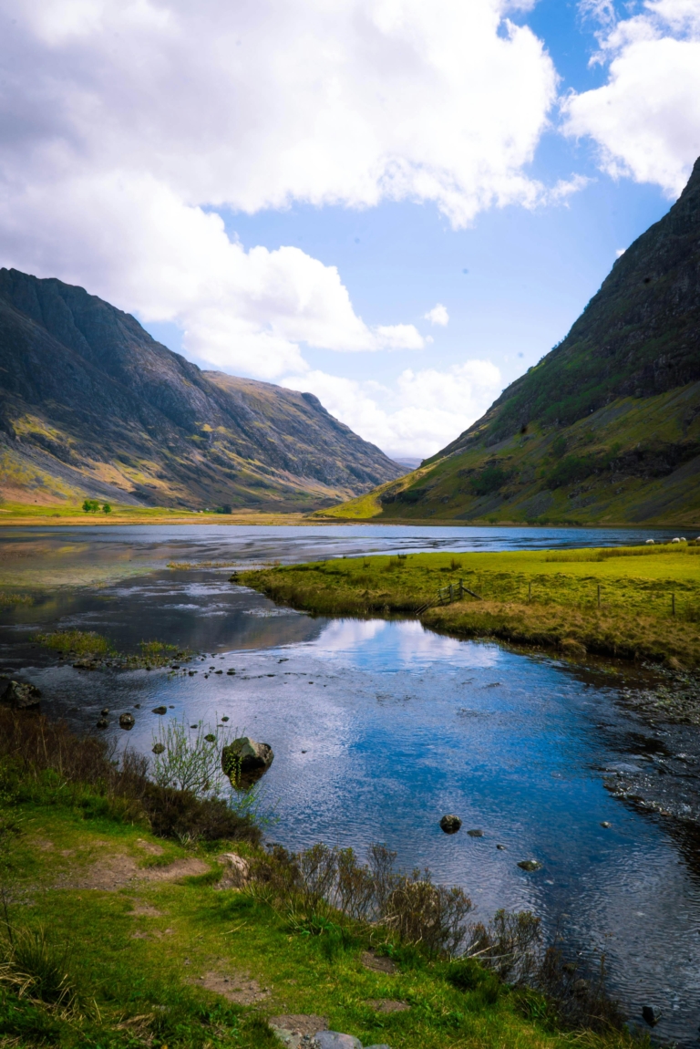 Breathtaking view of a valley with a reflective lake in the Scottish Highlands under a sunny sky.
