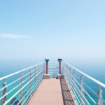 Experience the serenity of a sunny day on a coastal pier overlooking the tranquil sea.